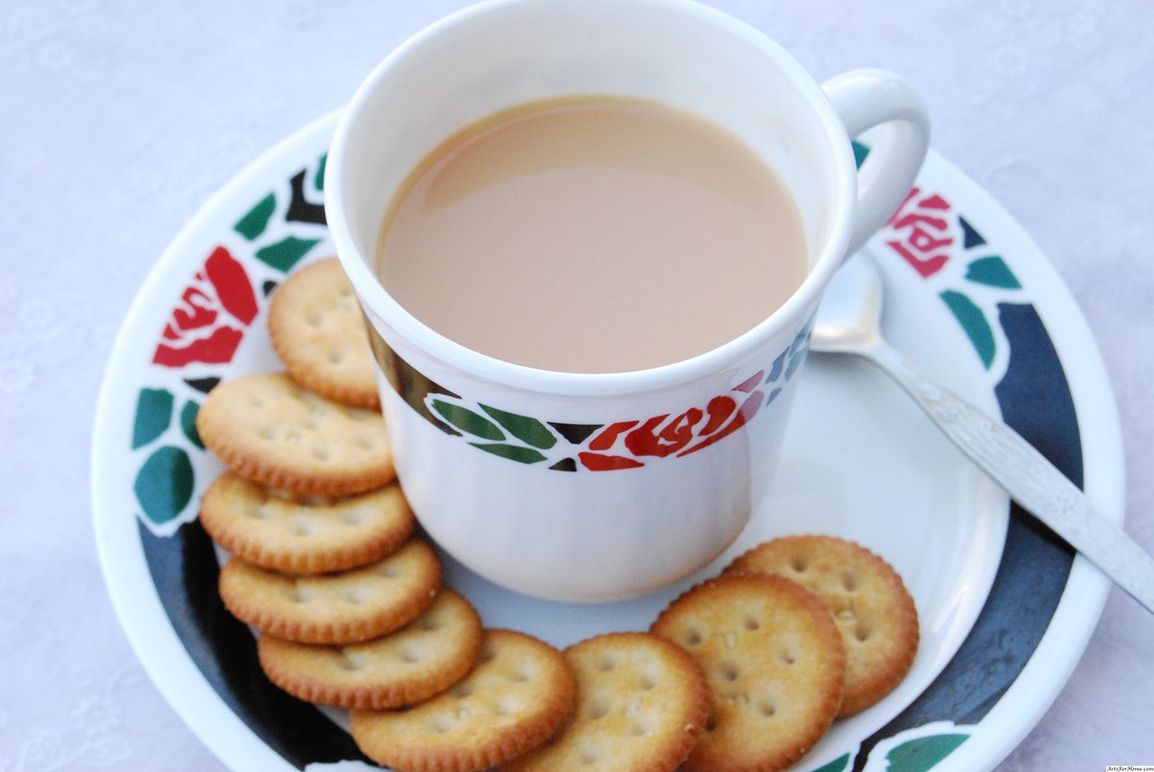 Cup of milky tea on a decorative saucer with round crackers, warm beige and cream tones, cozy mood